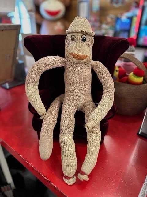 Luno, the real sock monkey, worn and faded, sitting in a tiny velvet armchair